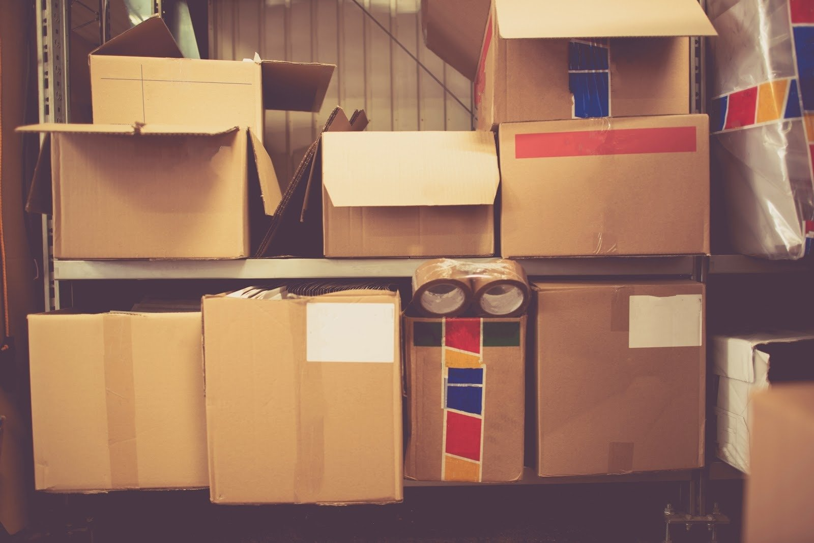 A drive-up self-storage unit with the roll up door open and boxes stacked inside it.